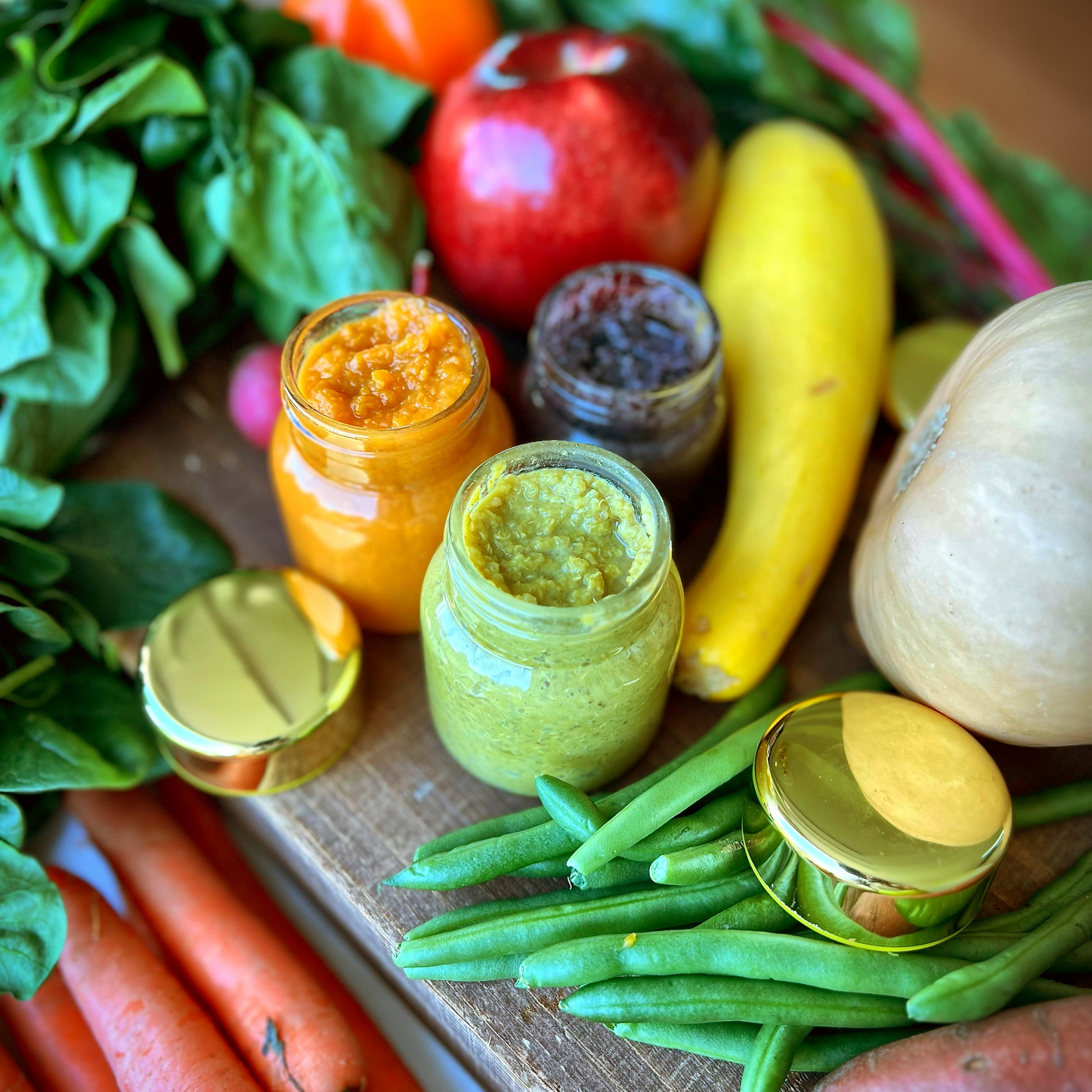 Chunky Vegan baby food jars with sweet potato, green bean, and purple sweet potato blends surrounded by fresh carrots, spinach, squash, apple, and beans. Plant-based infant and toddler meals made with locally sourced produce, preservative-free in Northern Virginia.