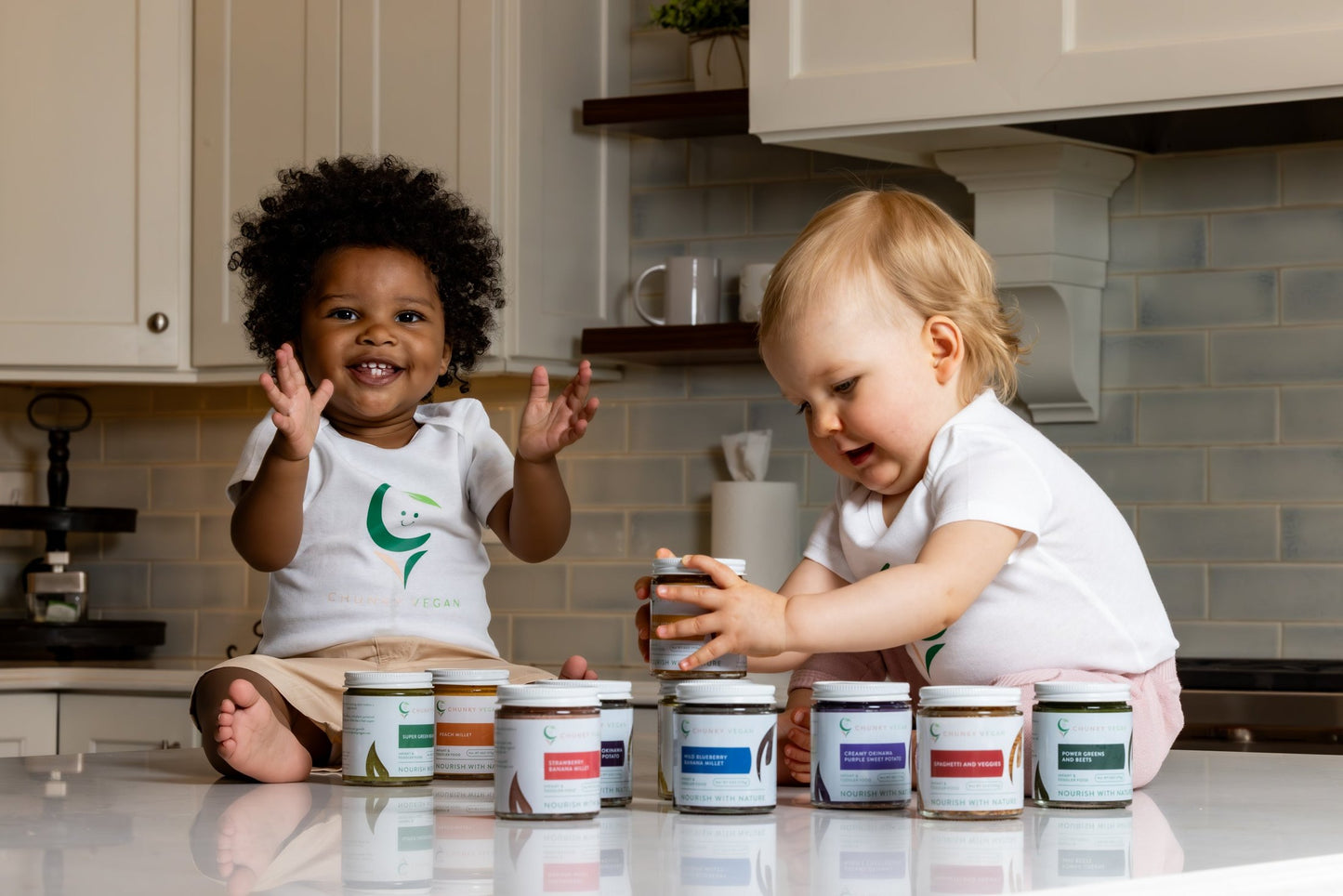 Two children in a kitchen with jars of Chunky Vegan baby food on the counter
